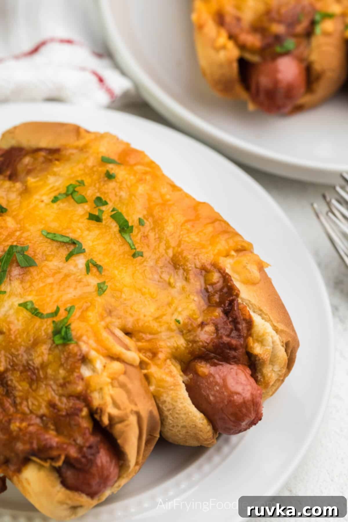 Crispy Air Fryer Chili Cheese Dogs 8 Delicious air fryer chili cheese dogs served on a white plate, garnished and ready to enjoy.