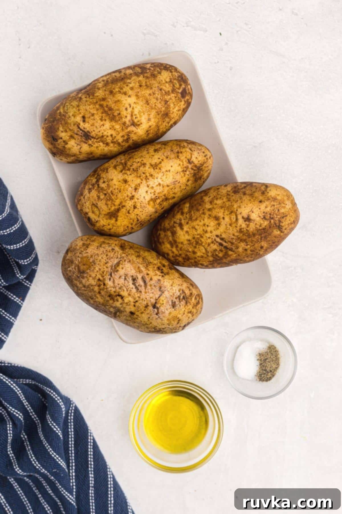 Revive Your Baked Potato in the Air Fryer 3 baked potatoes and oil and salt and pepper on a table.
