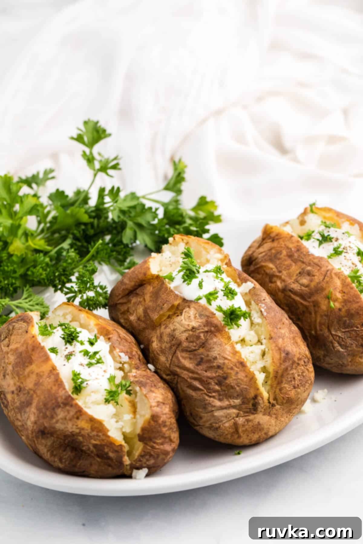 Revive Your Baked Potato in the Air Fryer 5 baked potatoes sliced open and topped with sour cream and fresh parsley.