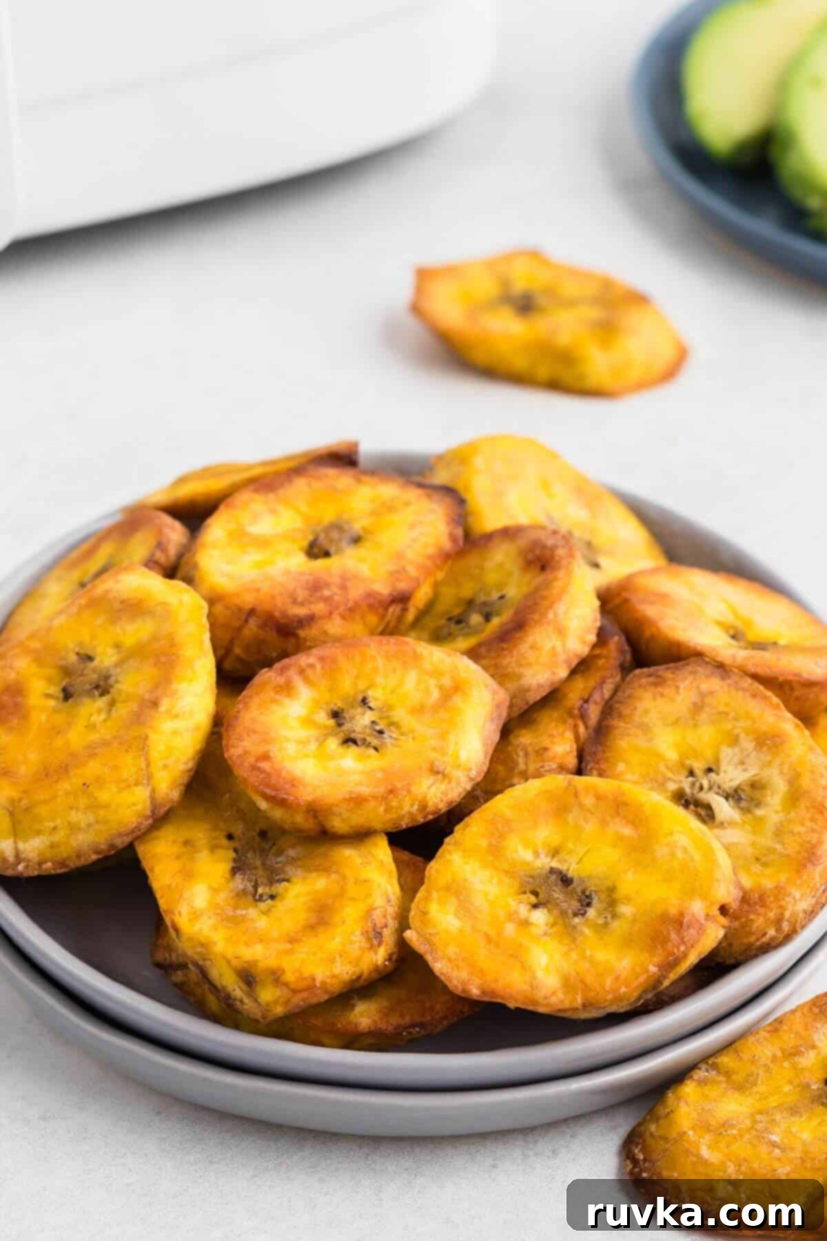 Sweet & Crispy Air Fryer Plantains 2 Golden plantain slices on a small plate in front of the air fryer.