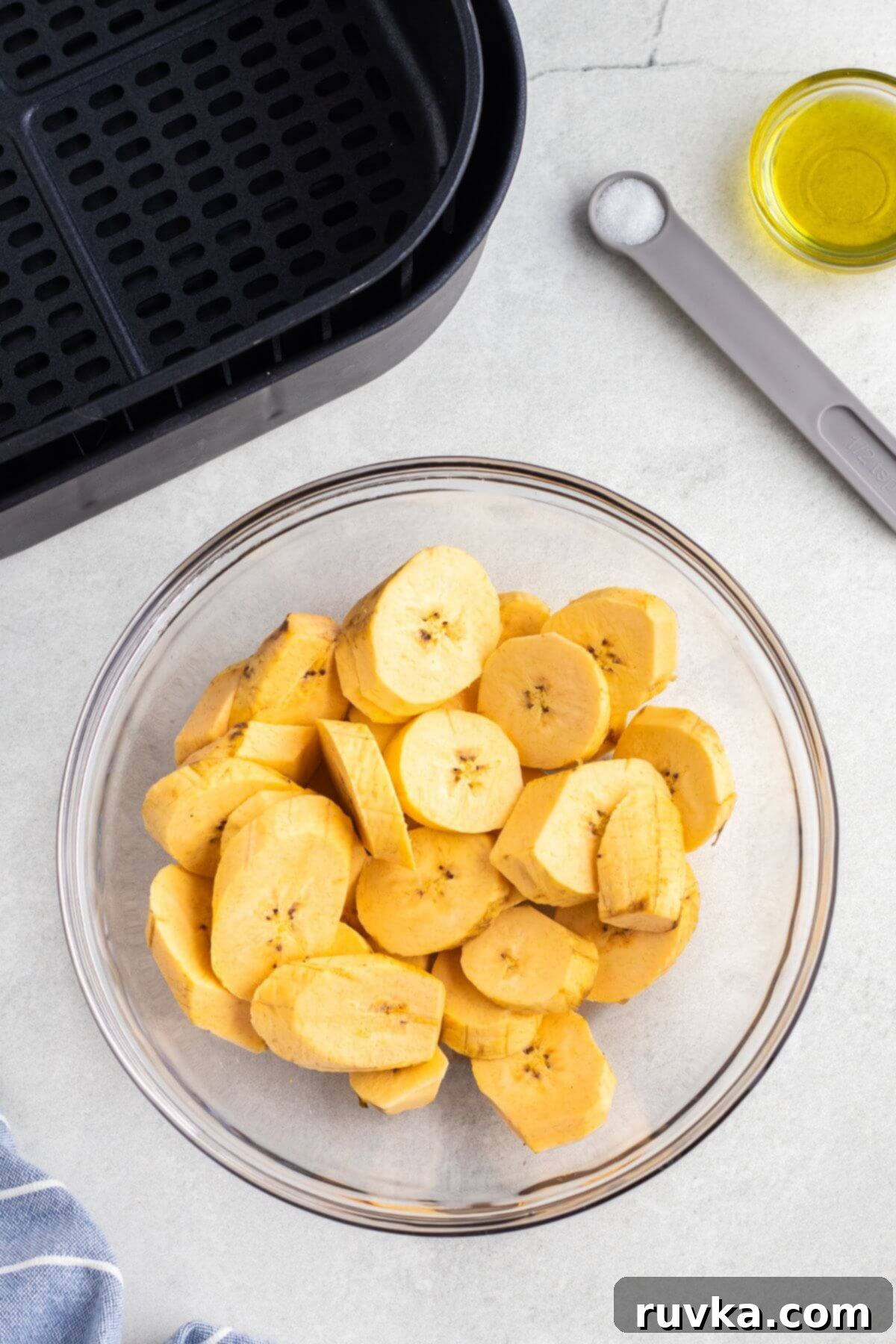Sweet & Crispy Air Fryer Plantains 5 Slices of plantains in a clear glass bowl after being tossed with olive oil
