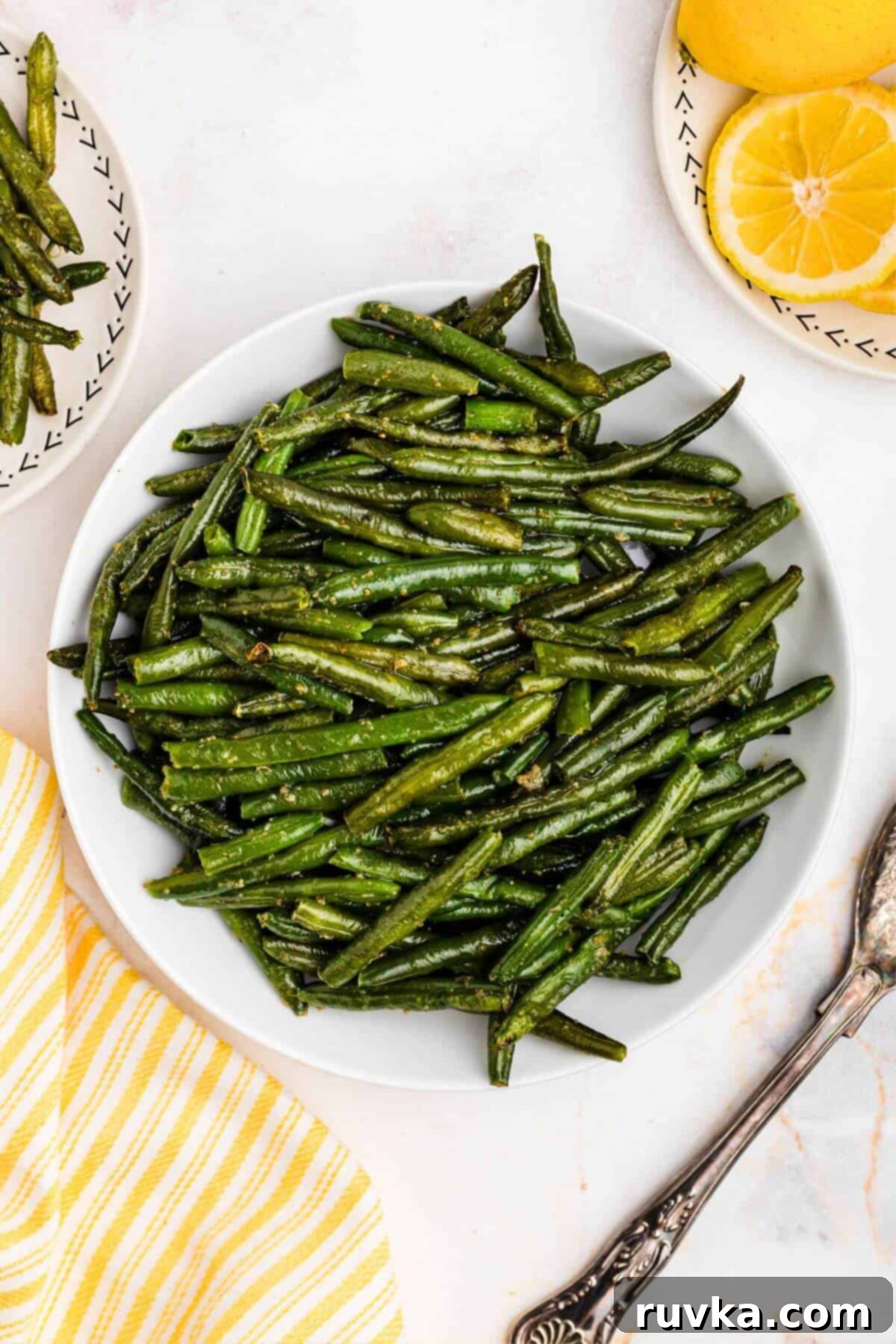 Crispy Air Fryer Frozen Green Beans 2 Juicy green green beans on a white plate next to a serving spoon.