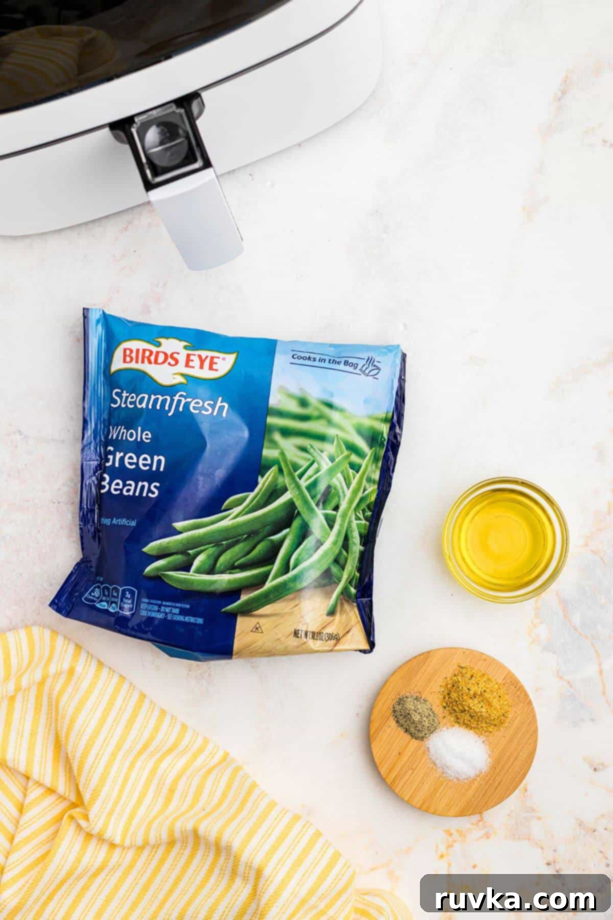 Crispy Air Fryer Frozen Green Beans 3 Bag of frozen green beans with olive oil and seasonings on a marble table.
