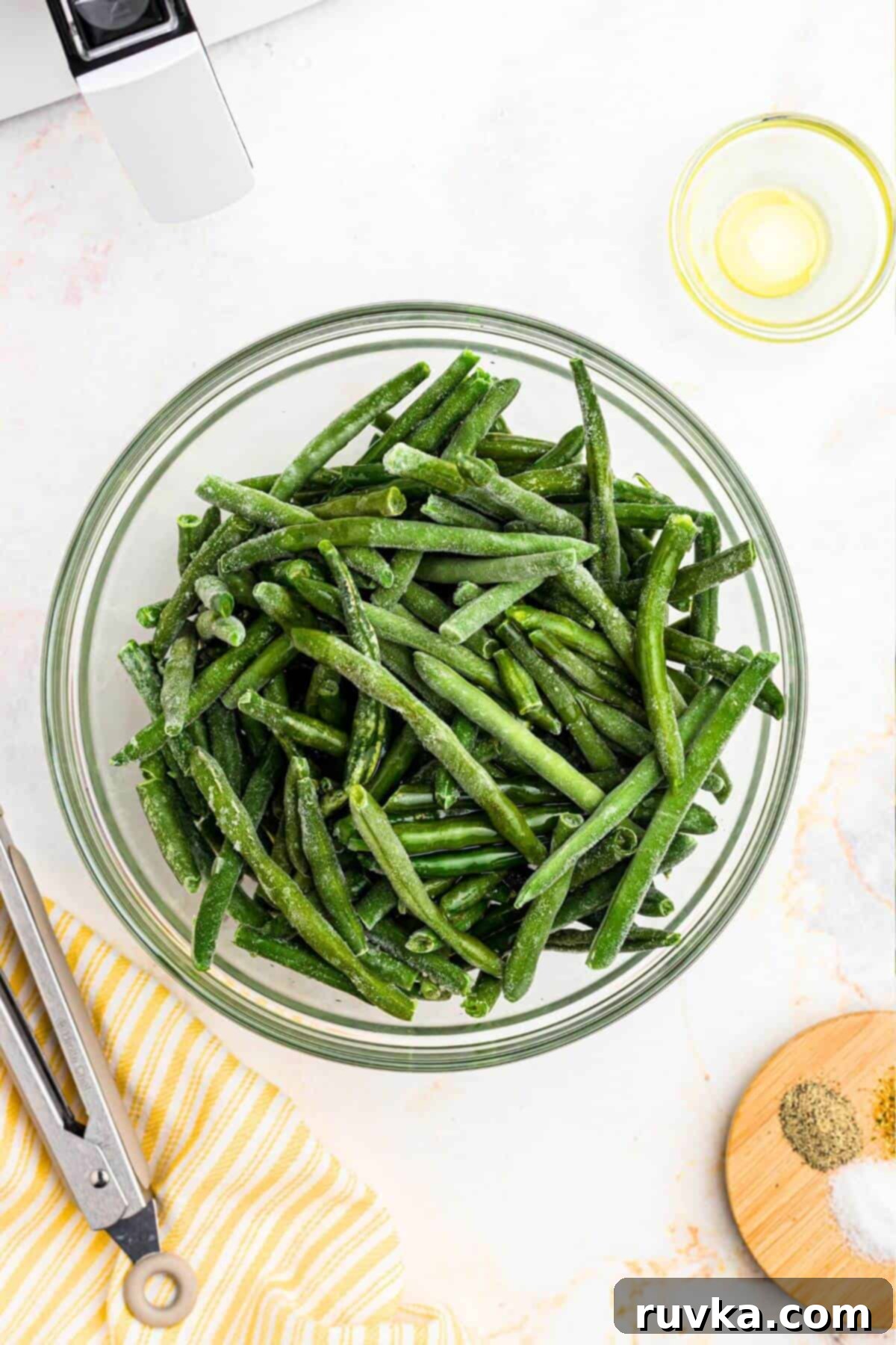 Crispy Air Fryer Frozen Green Beans 4 Frozen green beans in a glass bowl tossed with olive oil.