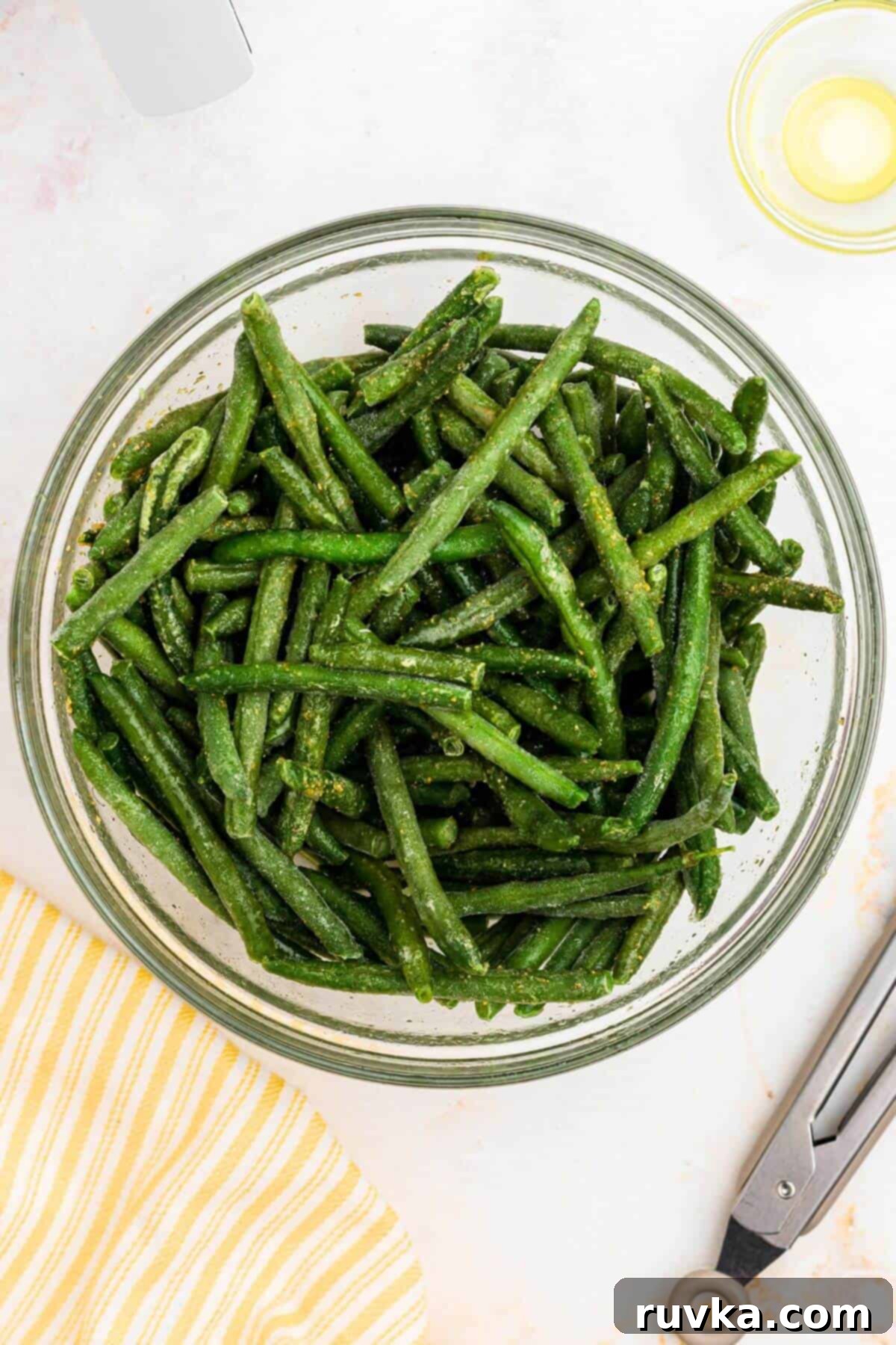 Crispy Air Fryer Frozen Green Beans 5 Frozen green beans in a clear glass bowl tossed with olive oil and seasonings.