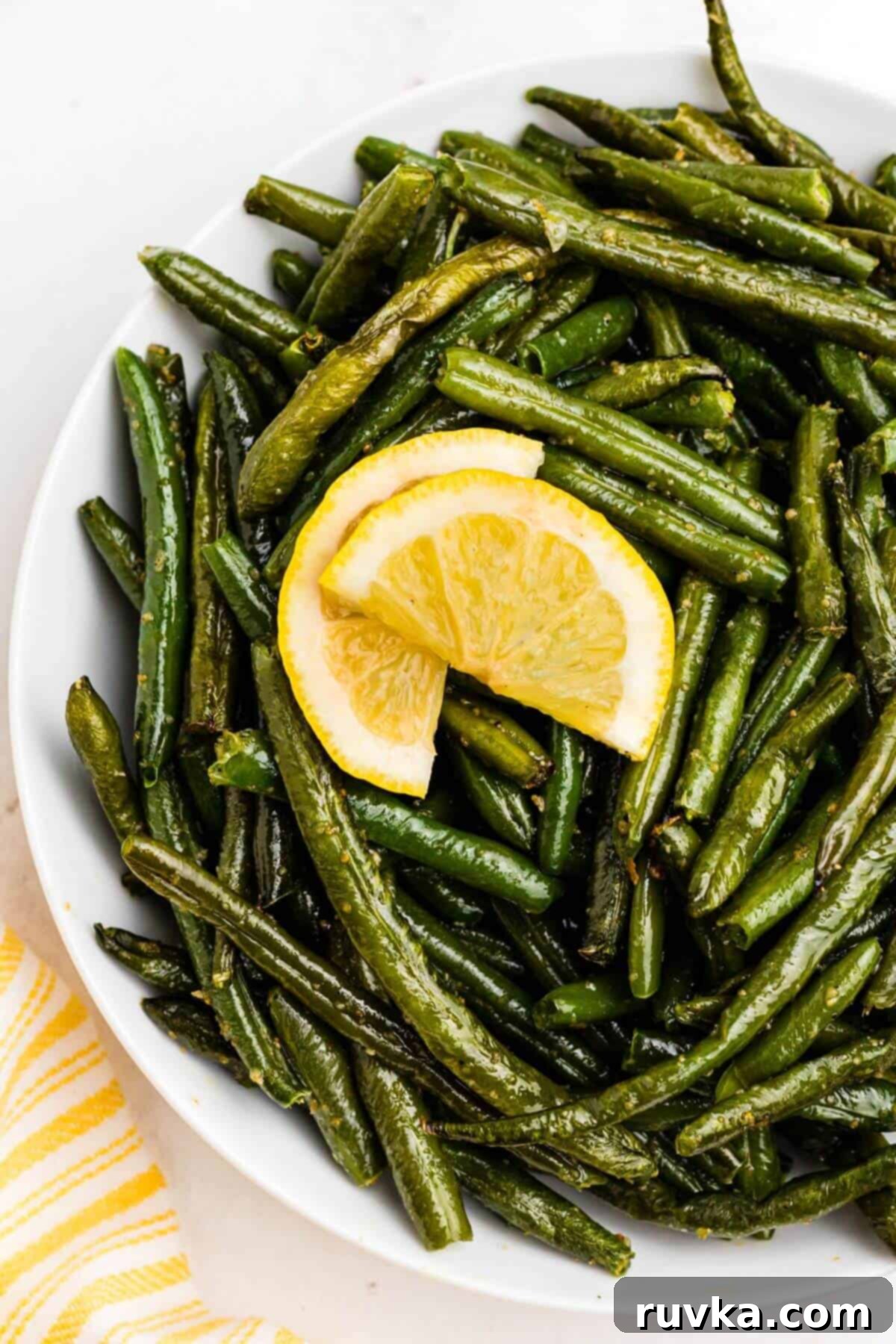Crispy Air Fryer Frozen Green Beans 8 Juicy green beans in a white bowl topped with lemon wedges.