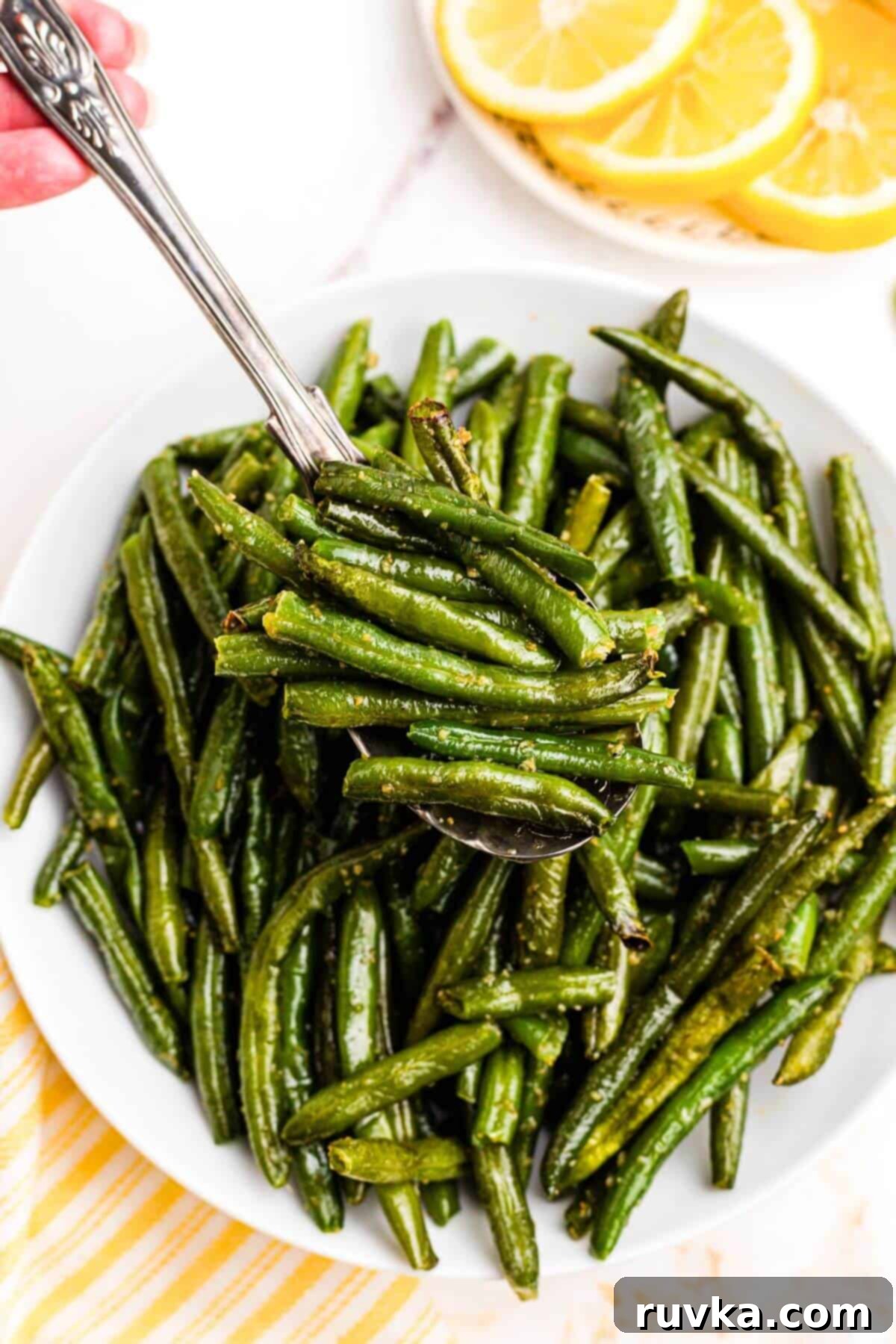 Crispy Air Fryer Frozen Green Beans 9 Spoon lifting juicy green beans out of bowl.
