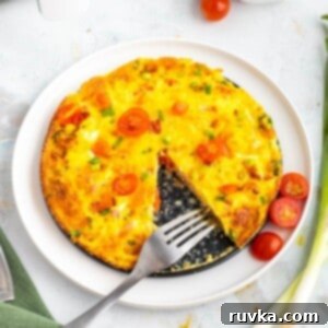 Easy Air Fryer Omelette 7 A beautifully fluffy air fryer omelette on a white plate, garnished with fresh herbs.