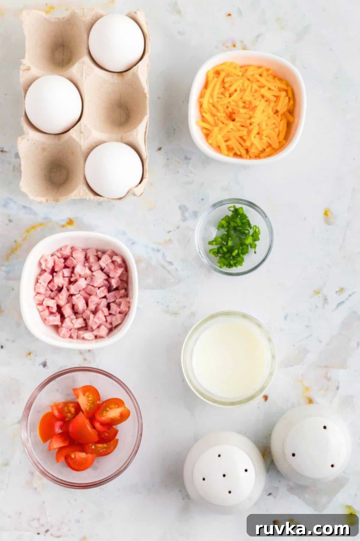 Easy Air Fryer Omelette 3 Fresh ingredients laid out on a kitchen counter, including eggs, milk, diced ham, shredded cheese, cherry tomatoes, and green onions, ready for an air fryer omelette.