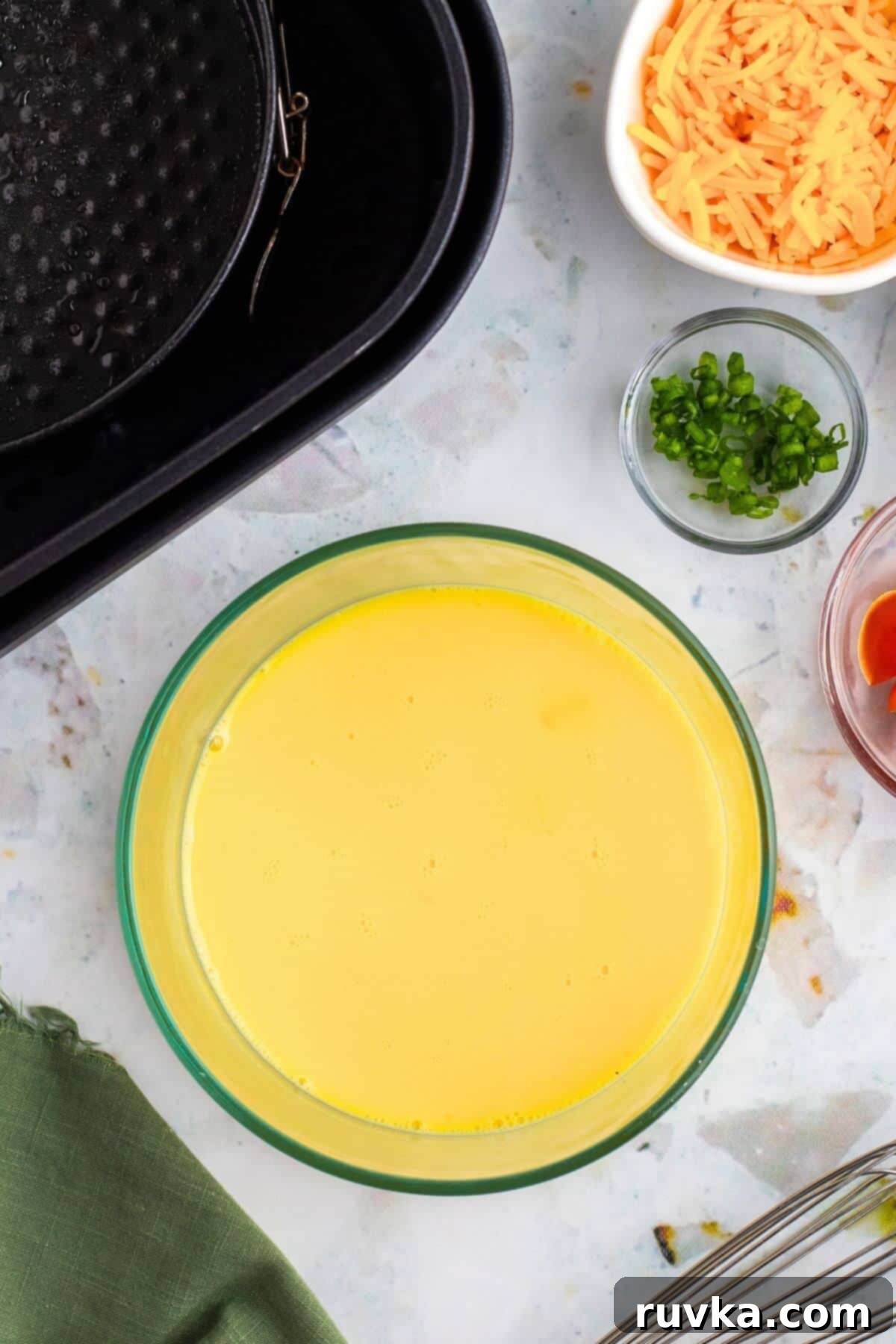 Easy Air Fryer Omelette 4 Egg yolks and whites, along with milk, perfectly whisked together in a clear glass bowl, ready for the next step of the omelette recipe.
