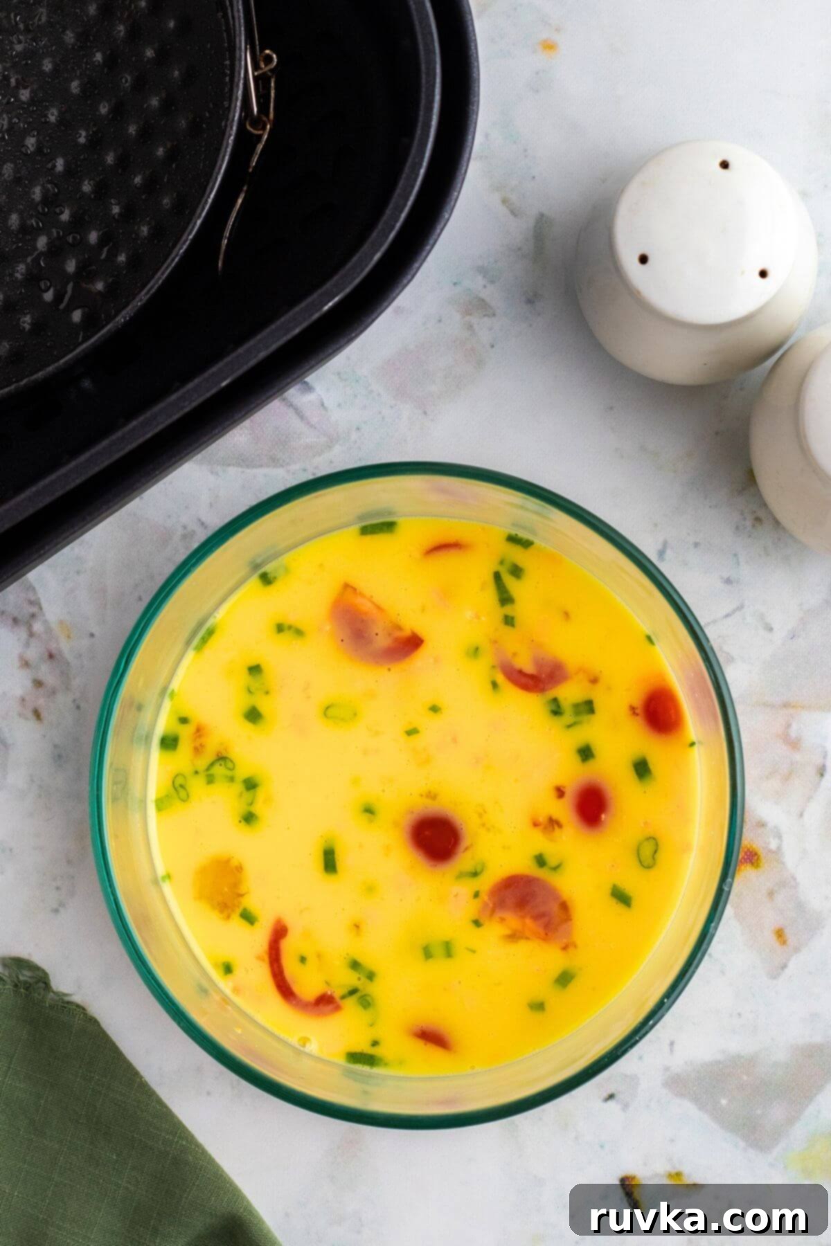 Easy Air Fryer Omelette 5 Diced ham, shredded cheese, chopped green onions, and diced tomatoes mixed into the whisked egg and milk mixture in a bowl for the omelette.