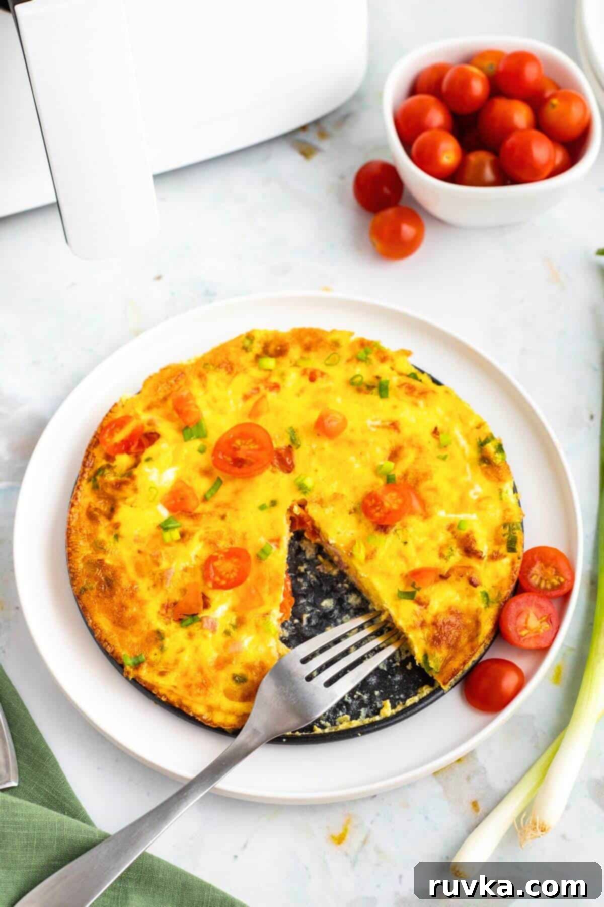 Easy Air Fryer Omelette 6 A perfectly cooked, fluffy yellow omelette, fresh from the air fryer, plated on a white dish with a sprinkle of green herbs.