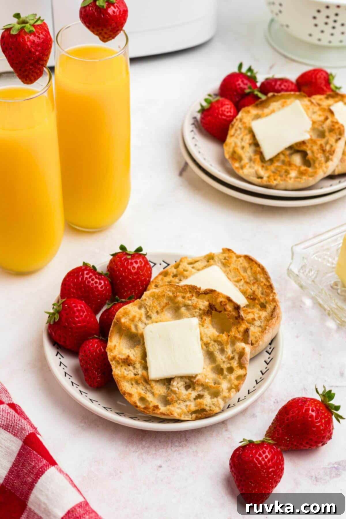 Homemade Air Fryer English Muffins 2 Golden crispy English muffins on a white plate served with strawberries and orange juice.