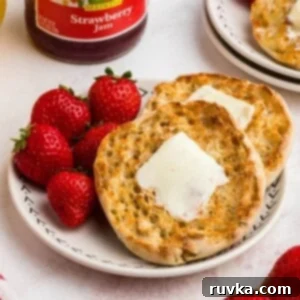 Homemade Air Fryer English Muffins 8 Golden crispy English muffins with a piece of butter on top, on a white plate served with strawberries and orange juice.
