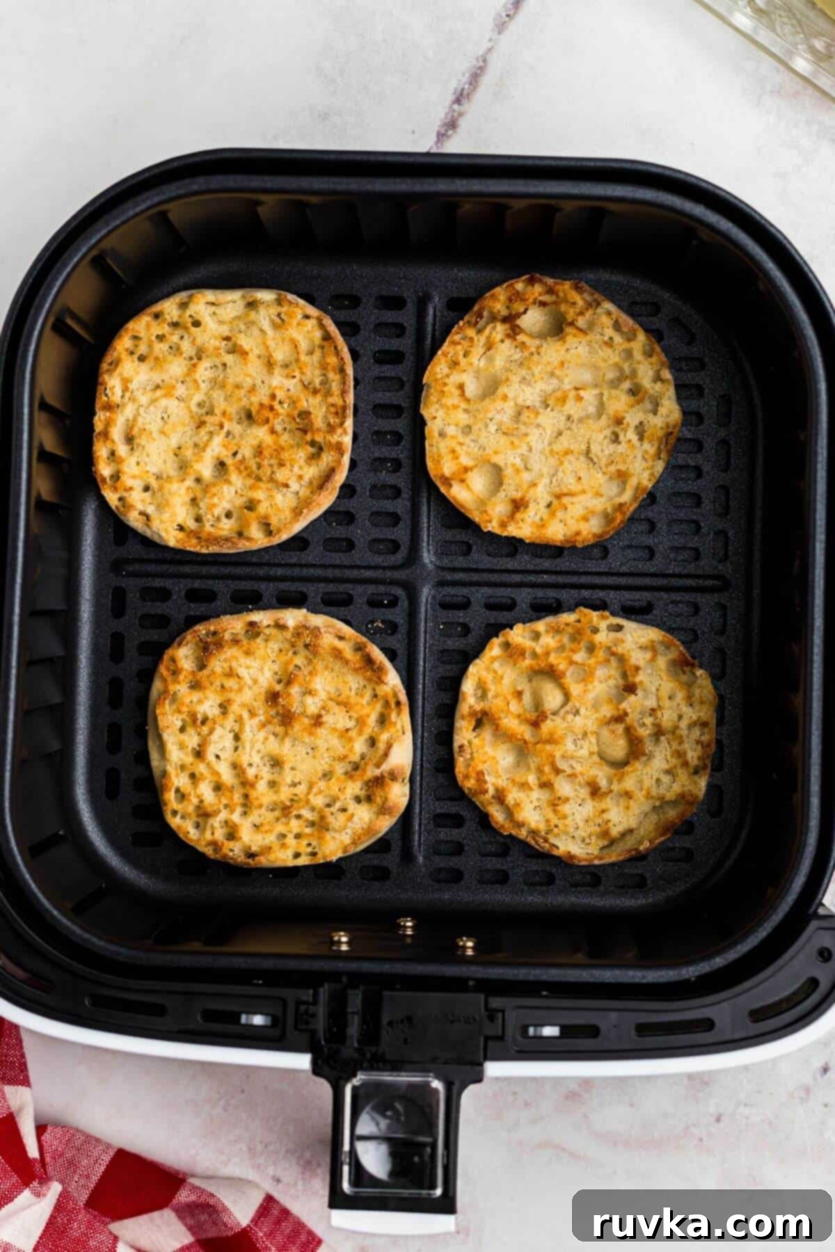 Homemade Air Fryer English Muffins 5 Golden crispy English muffins in the air fryer basket.