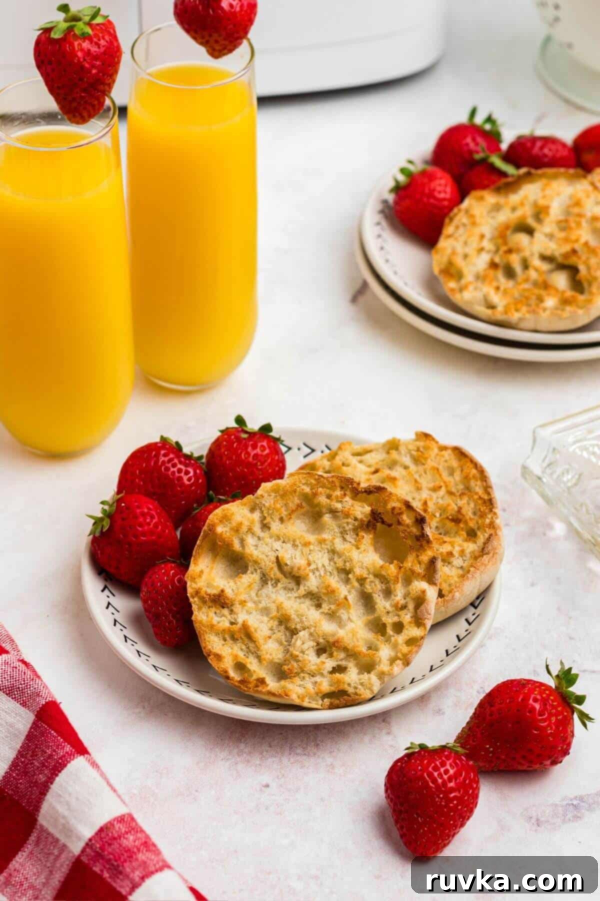 Homemade Air Fryer English Muffins 6 Golden crispy English muffins on a white plate served with strawberries and orange juice.