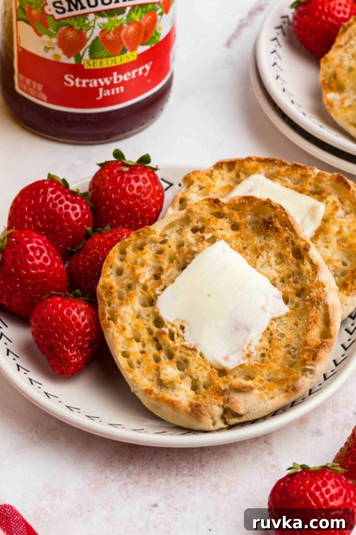 Homemade Air Fryer English Muffins 7 Golden crispy English muffins with a piece of butter on top, on a white plate served with strawberries and orange juice.