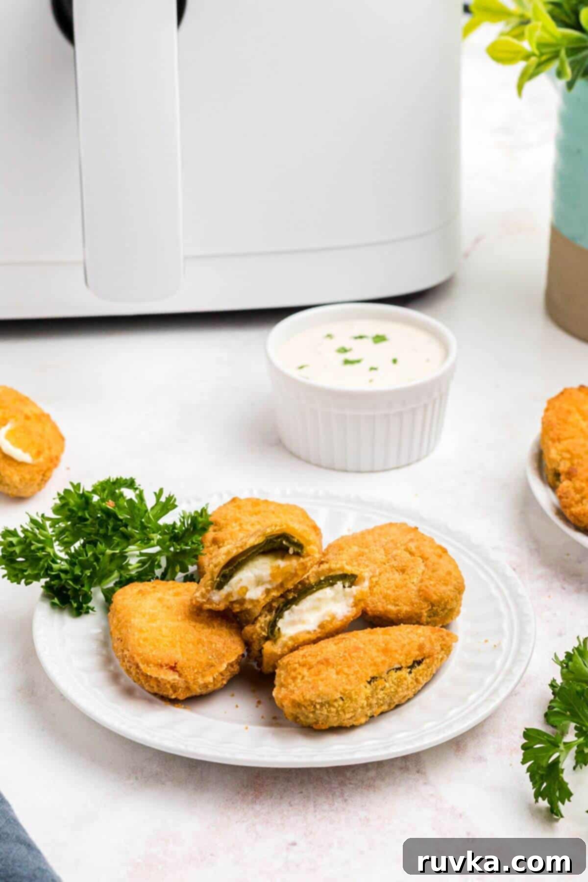 Crispy Air Fryer Frozen Jalapeno Poppers 2 Golden crispy breaded jalapeno poppers on a small white plate.