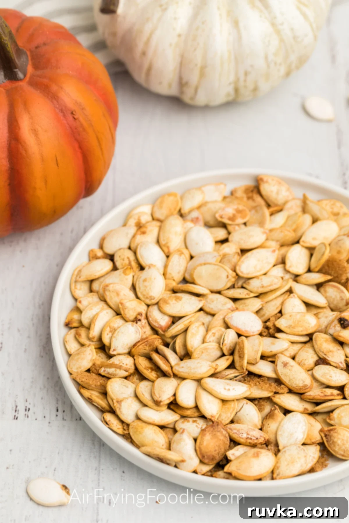15 Cozy Autumn Air Fryer Desserts You'll Adore 12 Pumpkin seeds made in the air fryer and served on a white plate with pumpkins surrounding them.