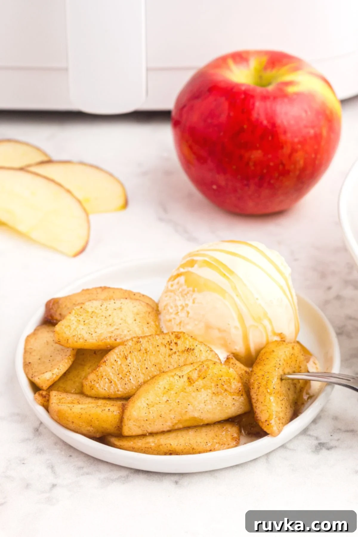 15 Cozy Autumn Air Fryer Desserts You'll Adore 16 Sliced apples cooked in the air fryer on a plate with a scoop of ice cream.