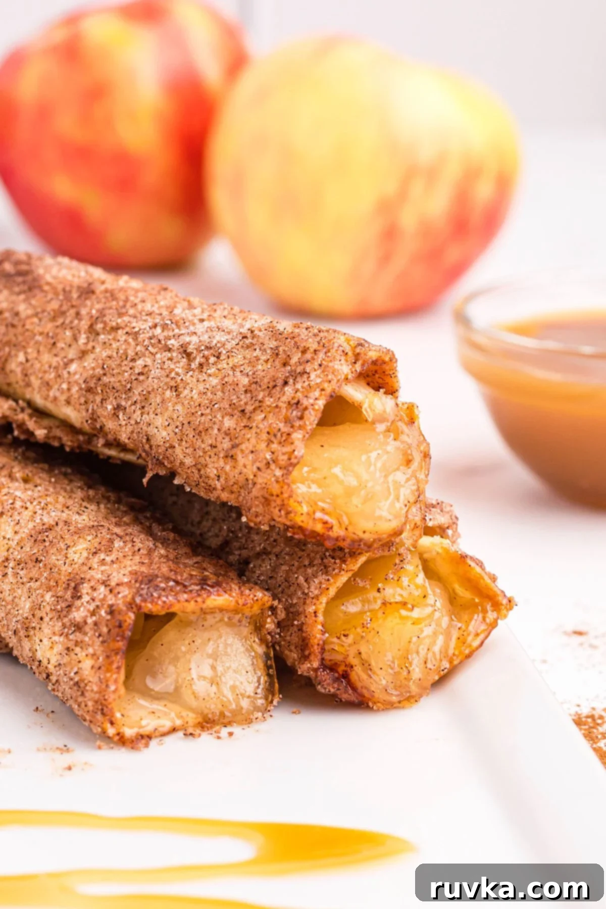 15 Cozy Autumn Air Fryer Desserts You'll Adore 9 Close up of apple pie taquitos on a white plate with apples in the background.