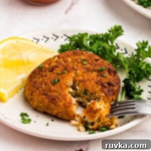 Crispy Air Fryer Frozen Crab Cakes 8 Golden crispy crab cake on a small white plate with a fork removing a bite and with a small bowl of cocktail sauce on the table for dipping.