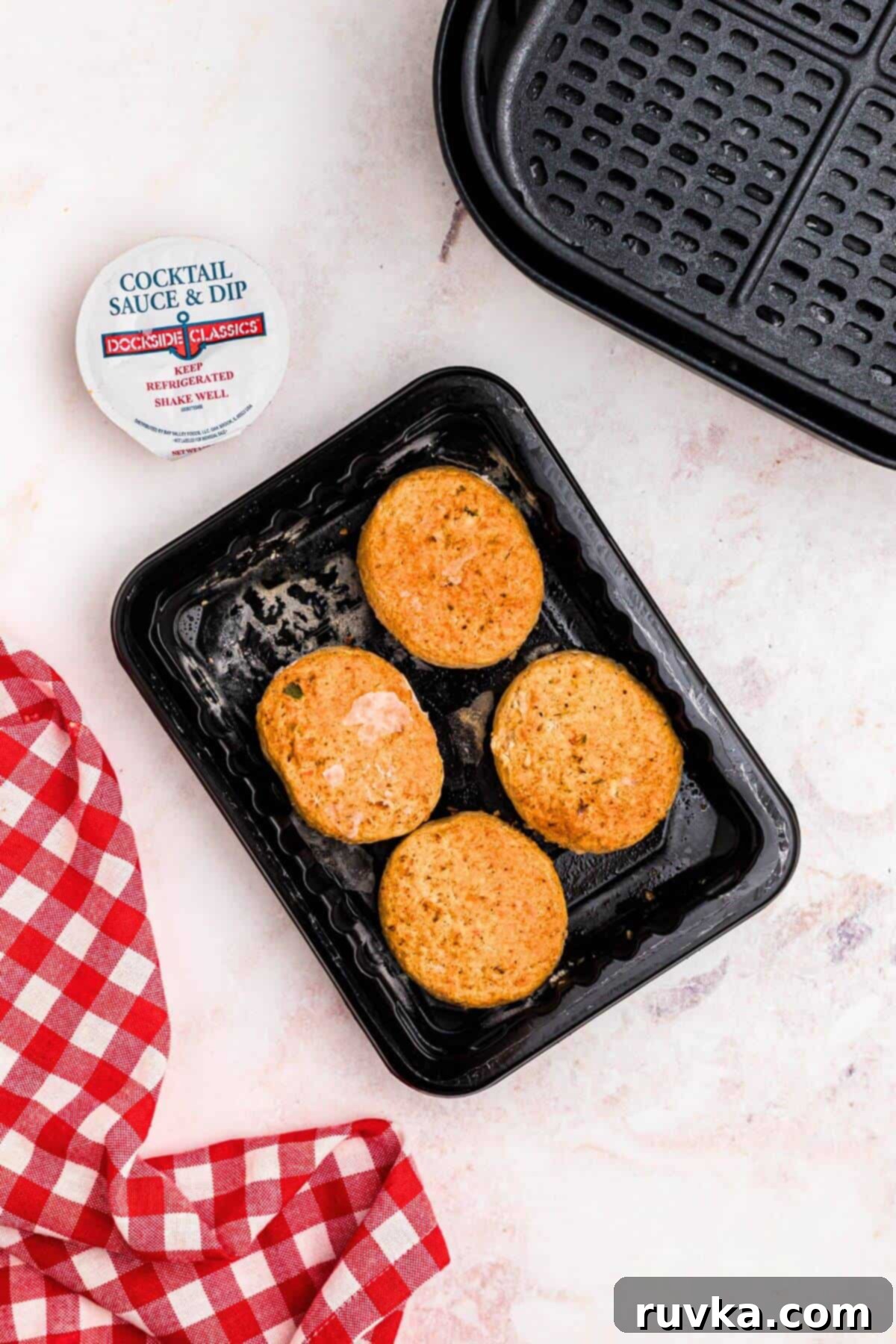 Crispy Air Fryer Frozen Crab Cakes 3 Frozen crab cakes on a black plastic plate in front of the air fryer basket.