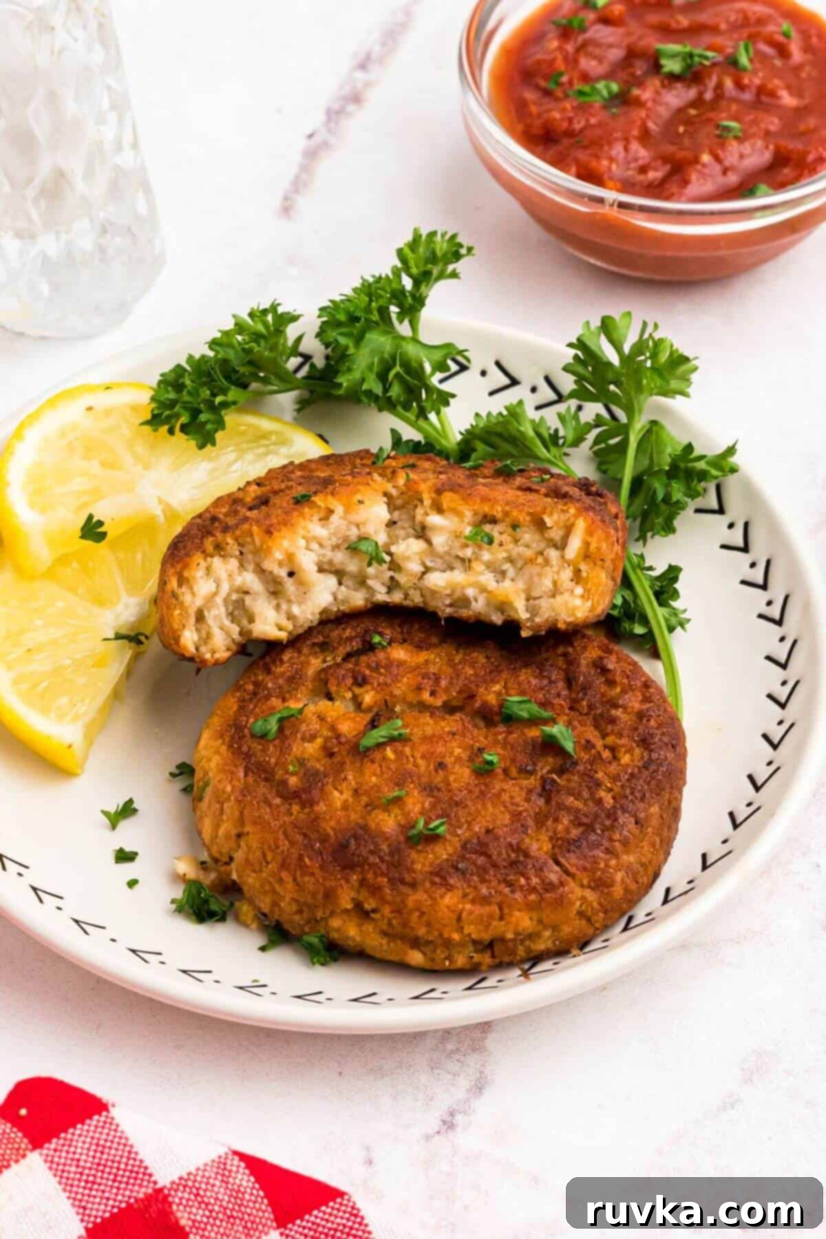 Crispy Air Fryer Frozen Crab Cakes 6 Golden crispy crab cakes on a small white plate with a small bowl of cocktail sauce on the table for dipping.