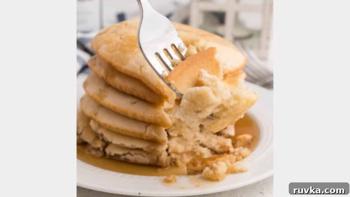 15 Effortless Breakfasts for a Perfect Start 7 Fluffy air fryer pancakes, stacked high and drizzled with syrup, with a fork taking a bite, served on a white plate, showcasing their perfect texture.