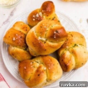 How to Air Fry Frozen Garlic Knots 9 Golden garlic knots on a white plate after being air fried, on a marble table.