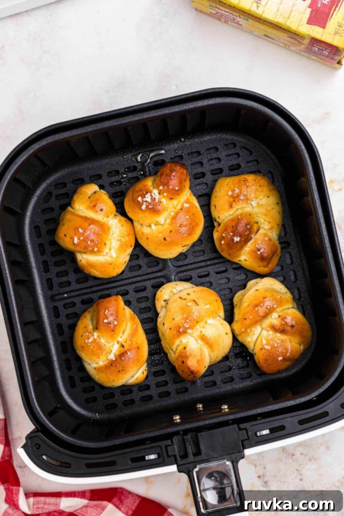 How to Air Fry Frozen Garlic Knots 5 Golden garlic knots topped with olive oil and cheese in the air fryer basket.