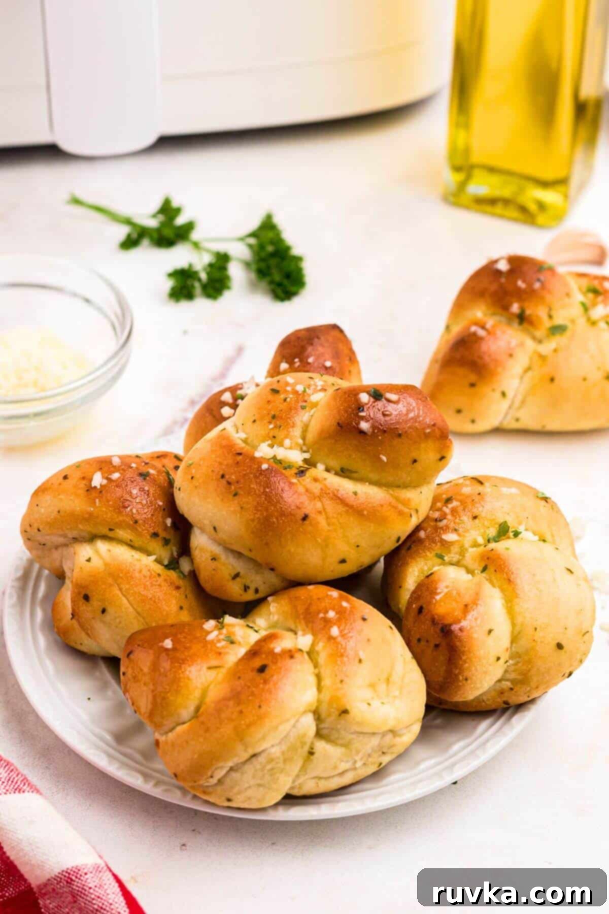 How to Air Fry Frozen Garlic Knots 8 Golden garlic knots on a white plate after being air fried, on a marble table with parsley garnish.
