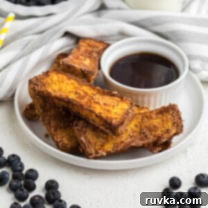 Golden Air Fryer French Toast Sticks 10 French toast sticks made in the air fryer on a white plate with blueberries surrounding it.