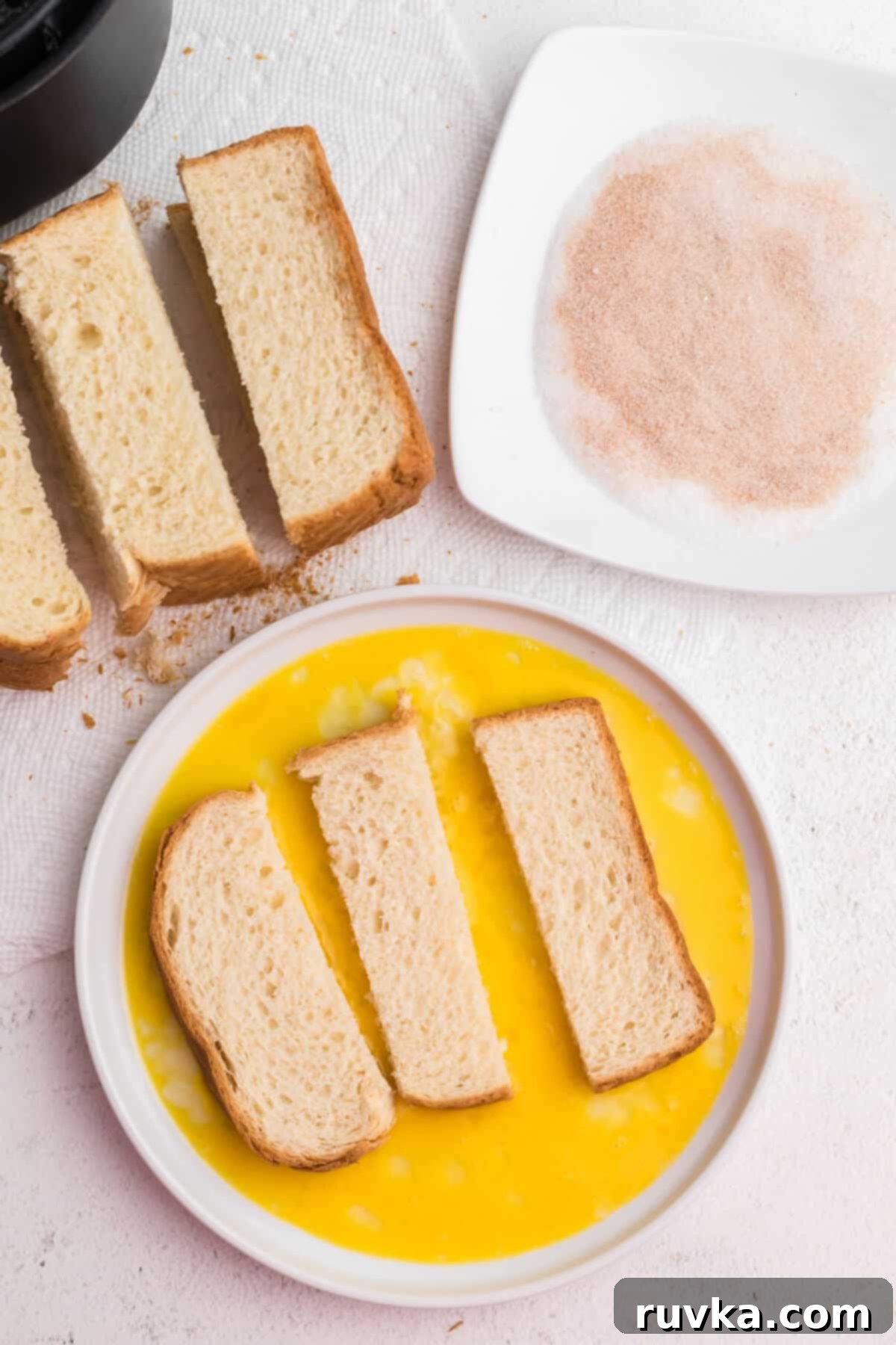 Golden Air Fryer French Toast Sticks 5 Bread sticks being dipped into the egg mixture before being placed into the air fryer basket.