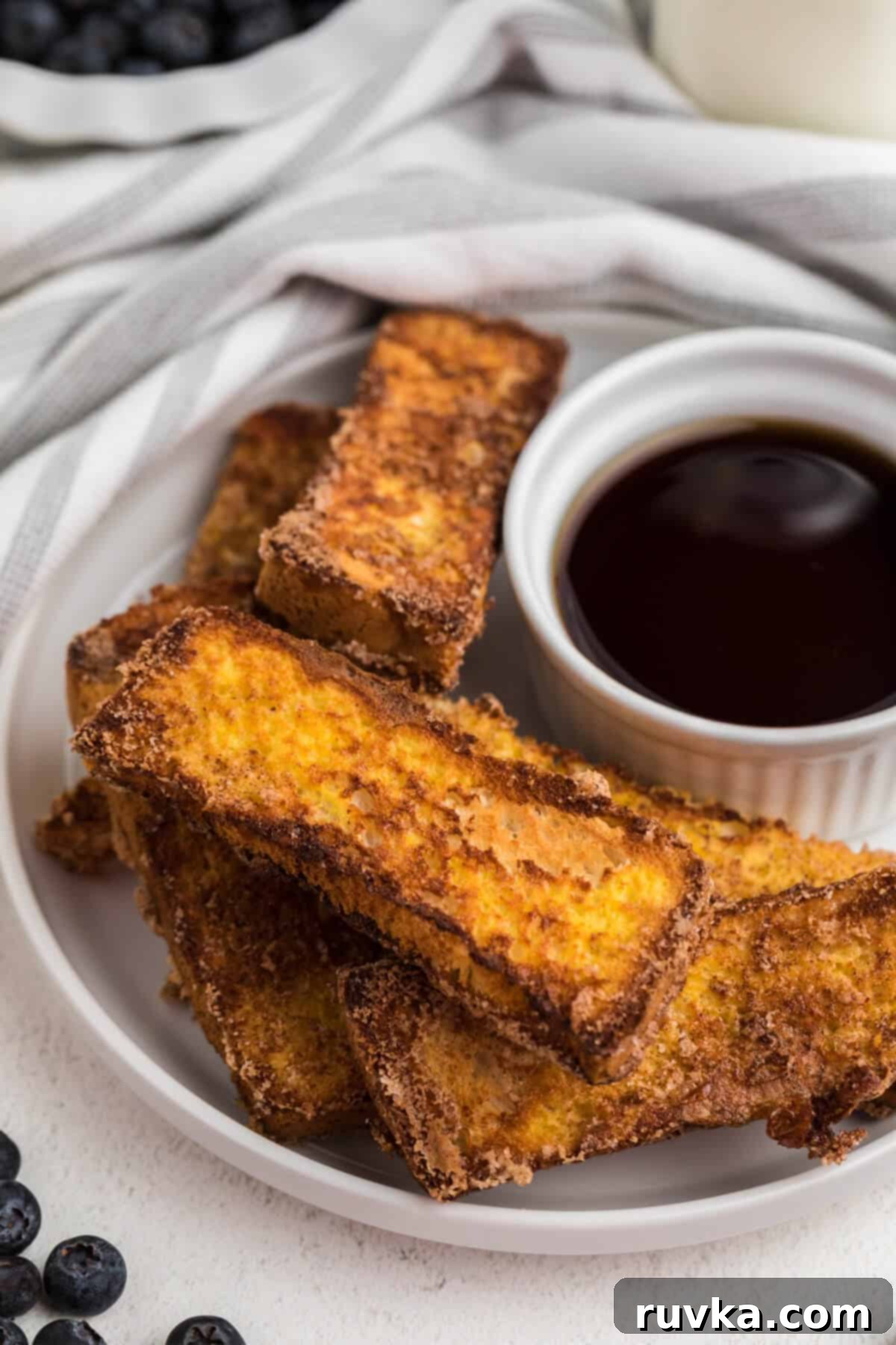 Golden Air Fryer French Toast Sticks 8 french toast sticks made in air fryer basket served on a a white plate with syrup for dipping.