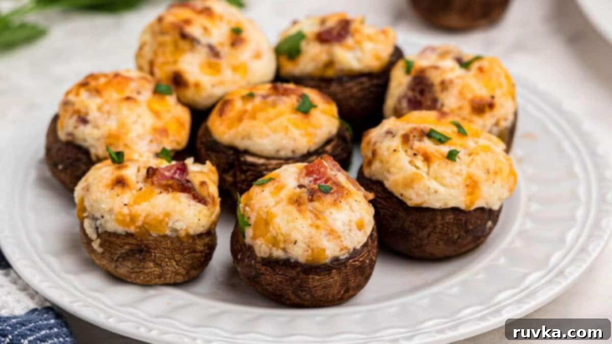 Epic Tailgate Bites Your Friends Will Love 8 stuffed mushrooms made in the air fryer and placed on a white plate, ready to serve.