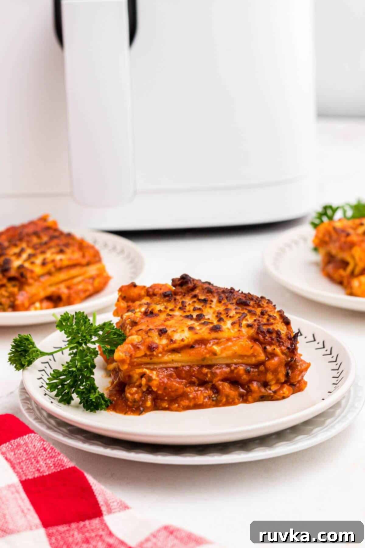 Perfect Air Fryer Frozen Lasagna 2 Cheesy cooked slice of lasagna with sauce on a white plate garnished with parsley.