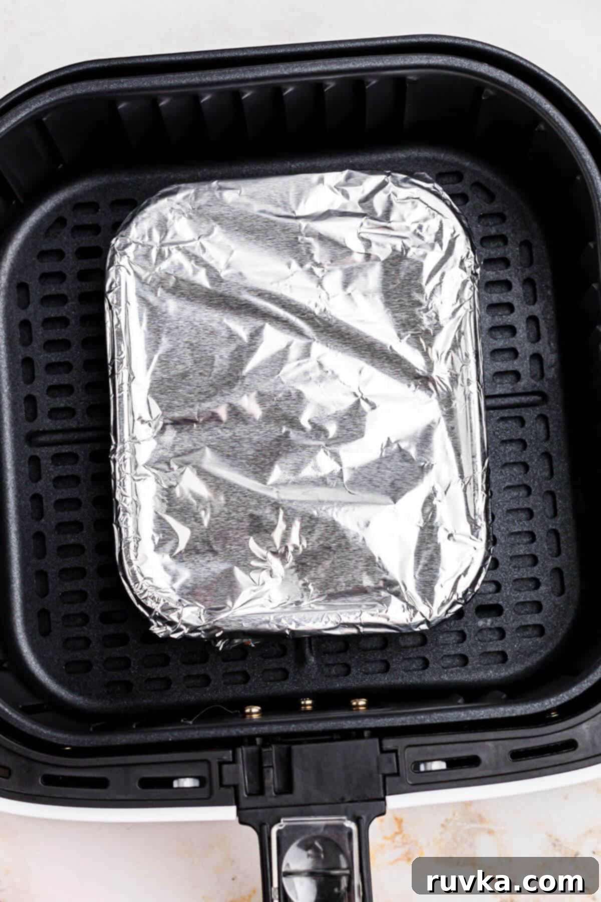 Perfect Air Fryer Frozen Lasagna 4 Frozen lasagna wrapped in a piece of aluminum foil, in the air fryer basket.