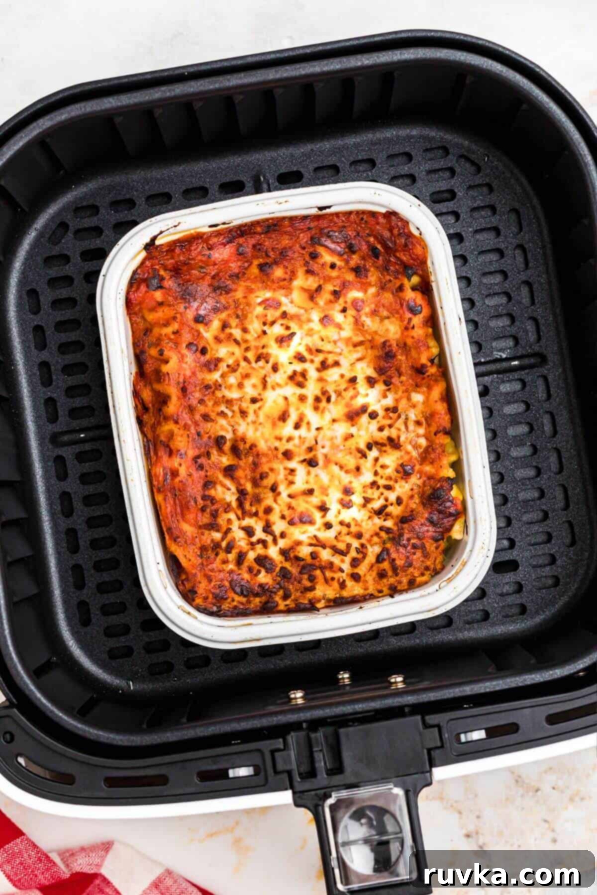 Perfect Air Fryer Frozen Lasagna 5 golden orange lasagna in a small tray in the air fryer basket after being cooked.