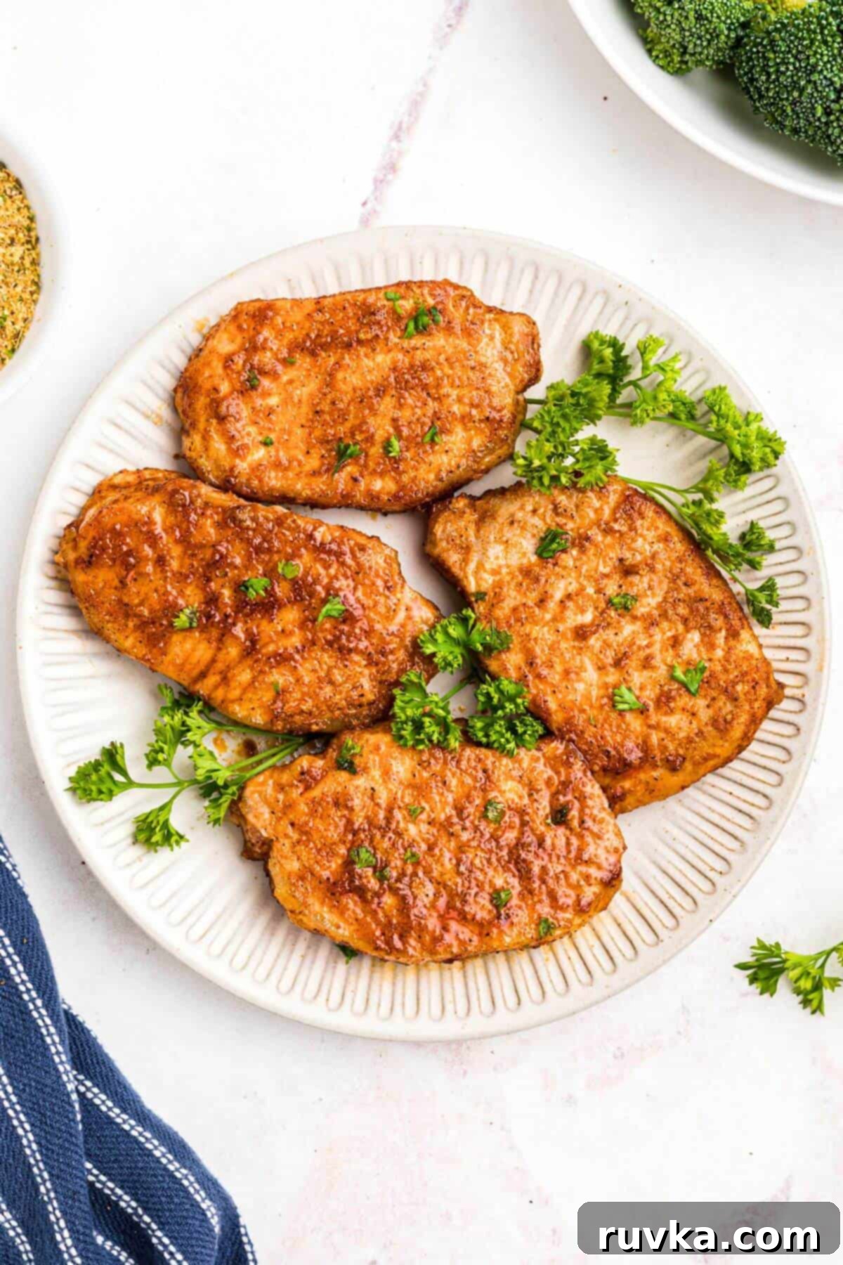 No-Thaw Air Fryer Pork Chops 2 Golden juicy and seasoned pork chops on a white plate with parsley garnish.