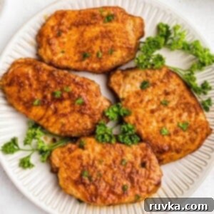 No-Thaw Air Fryer Pork Chops 10 Golden juicy and seasoned pork chops on a white plate with parsley garnish.