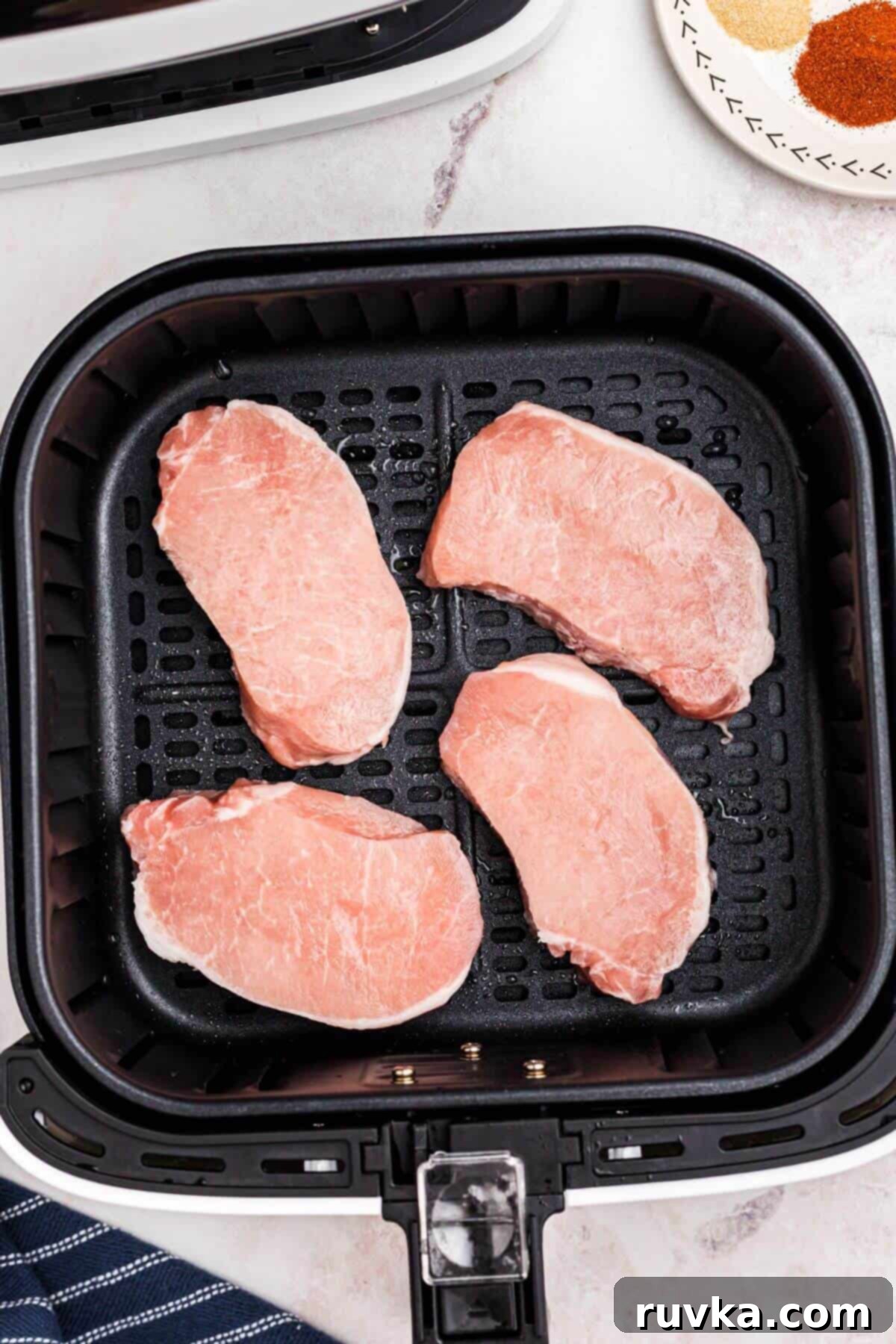 No-Thaw Air Fryer Pork Chops 4 Frozen pork chops in air fryer basket before being air fried.