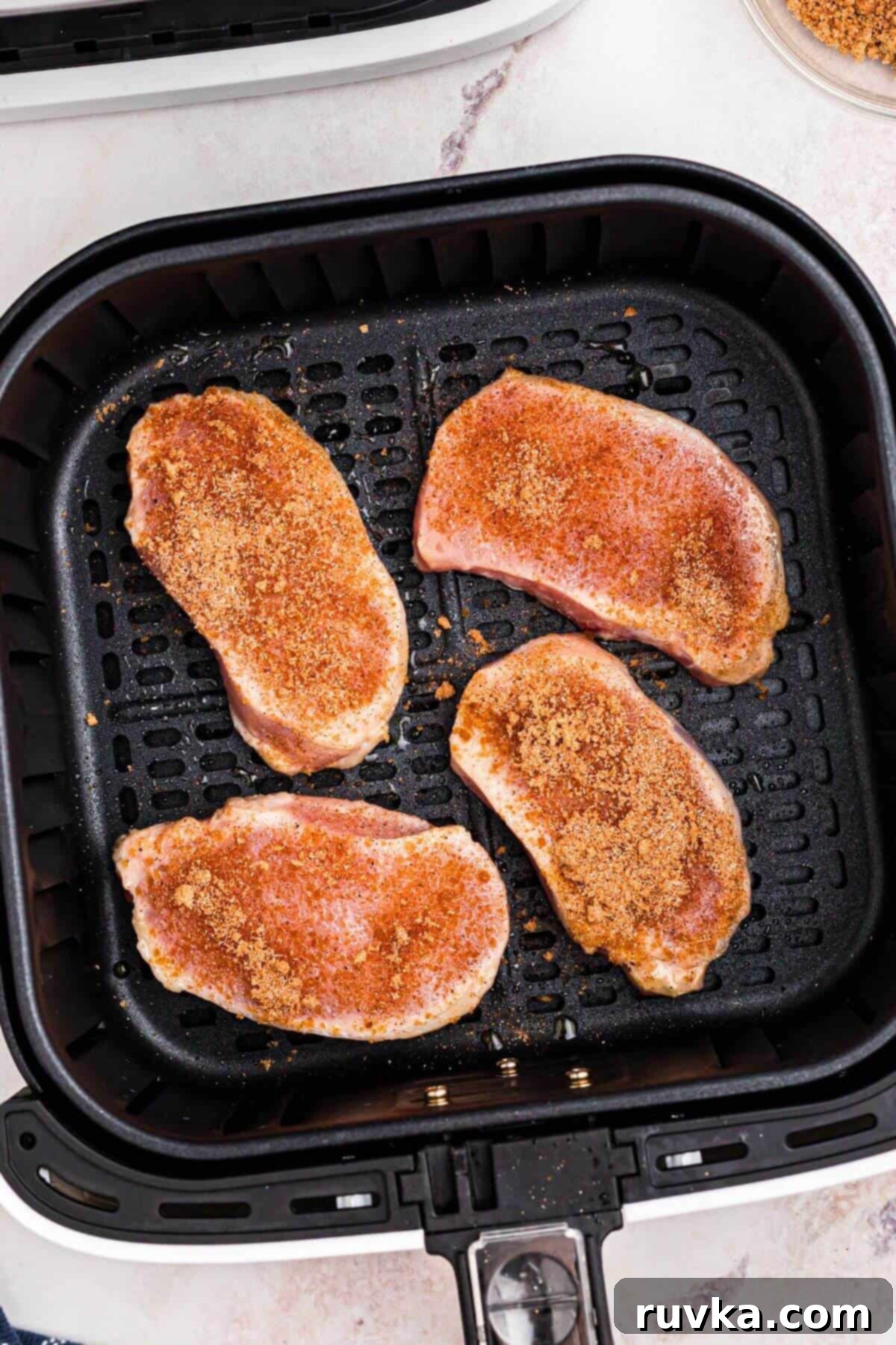 No-Thaw Air Fryer Pork Chops 7 Uncooked pork chops in the air fryer, seasoned.