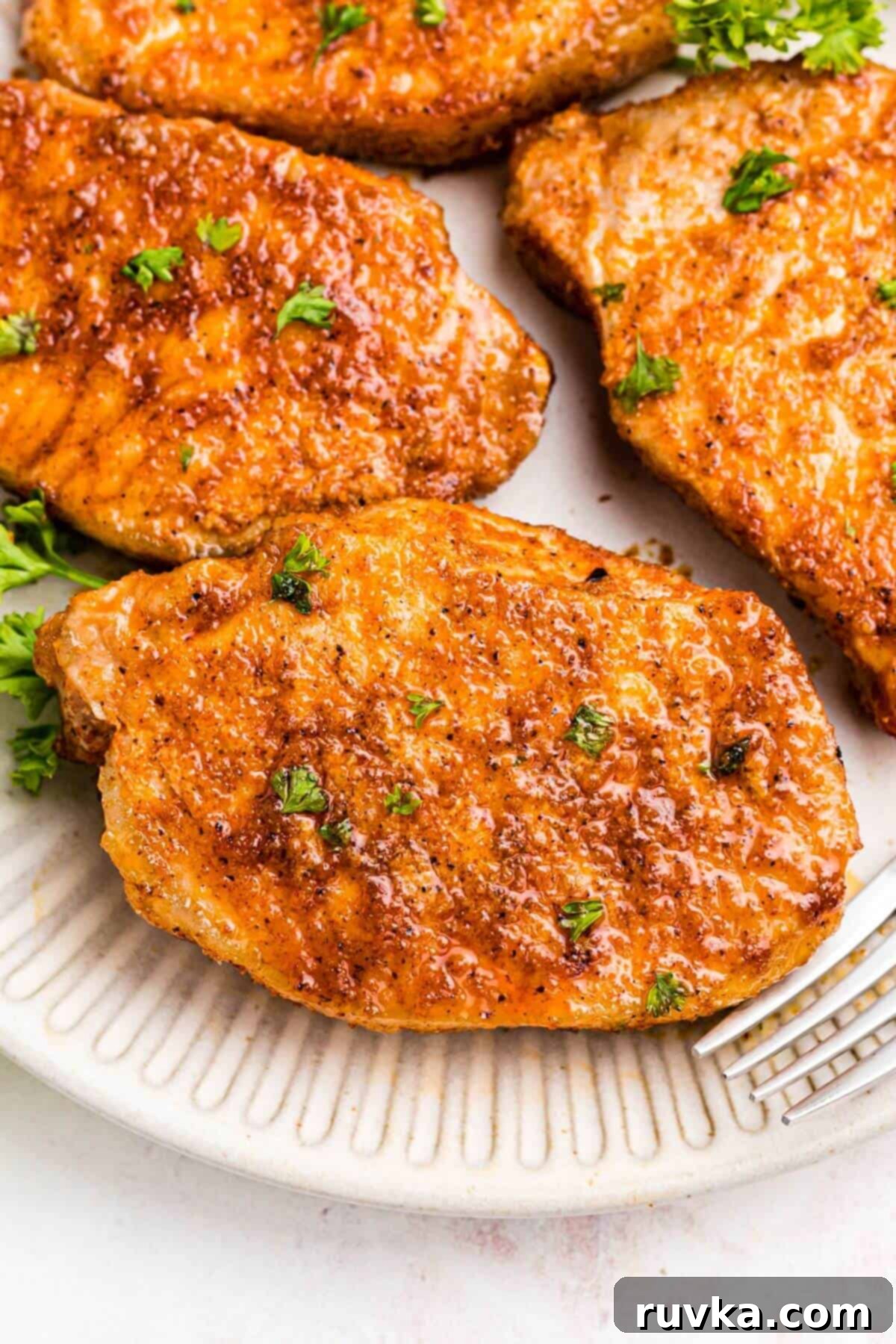 No-Thaw Air Fryer Pork Chops 9 Golden seasoned pork chops on a white plate with a fork and parsley garnish.