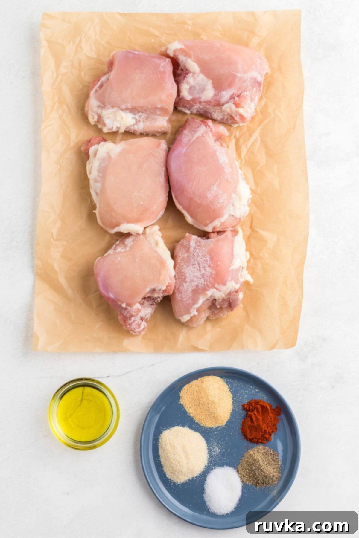 Freezer to Fabulous Air Fryer Chicken Thighs 3 Uncooked chicken thighs, seasonings, and olive oil measured out on a table.