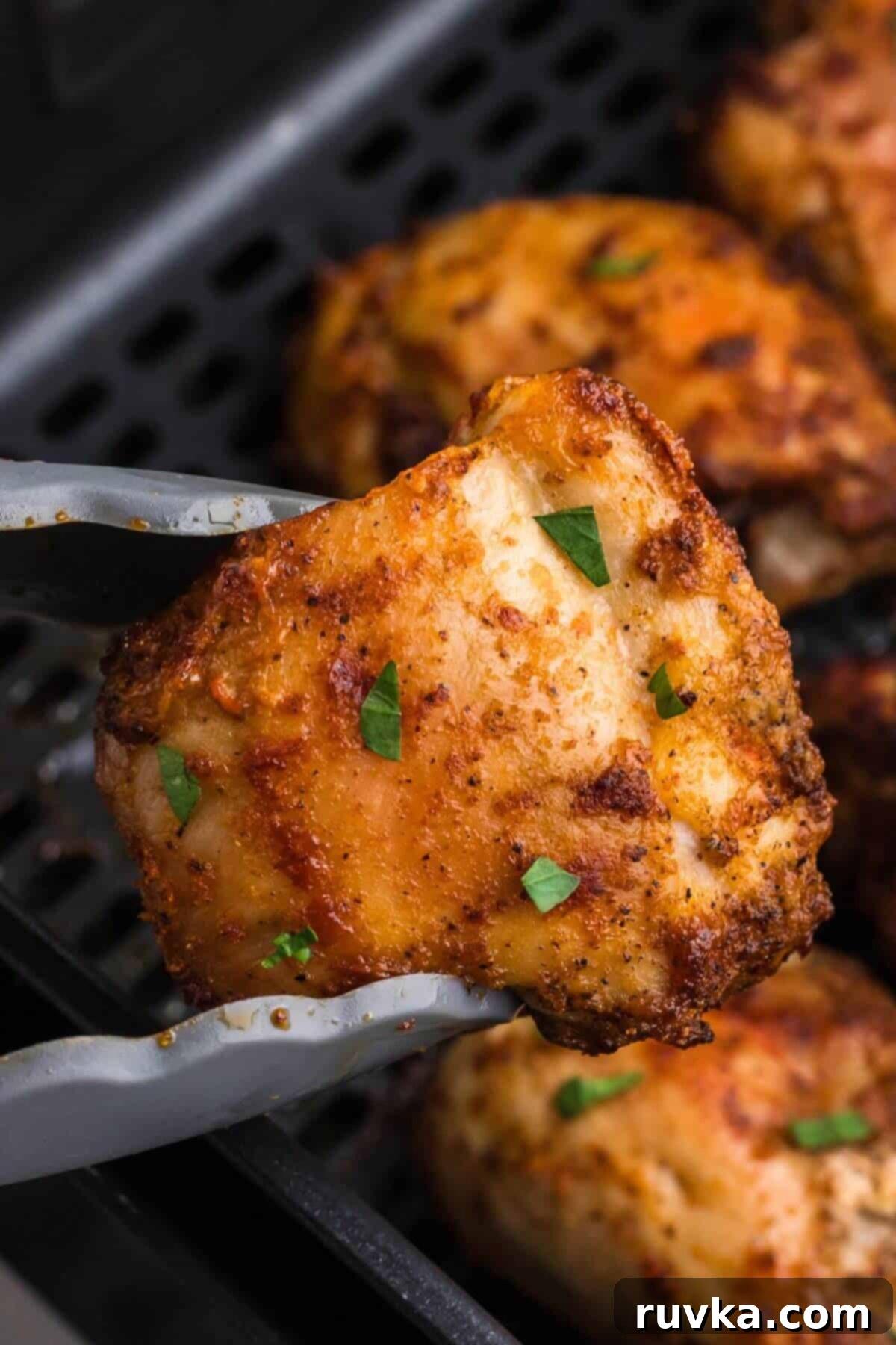 Freezer to Fabulous Air Fryer Chicken Thighs 7 Crispy golden chicken thighs in the air fryer basket with one being lifted with tongs.