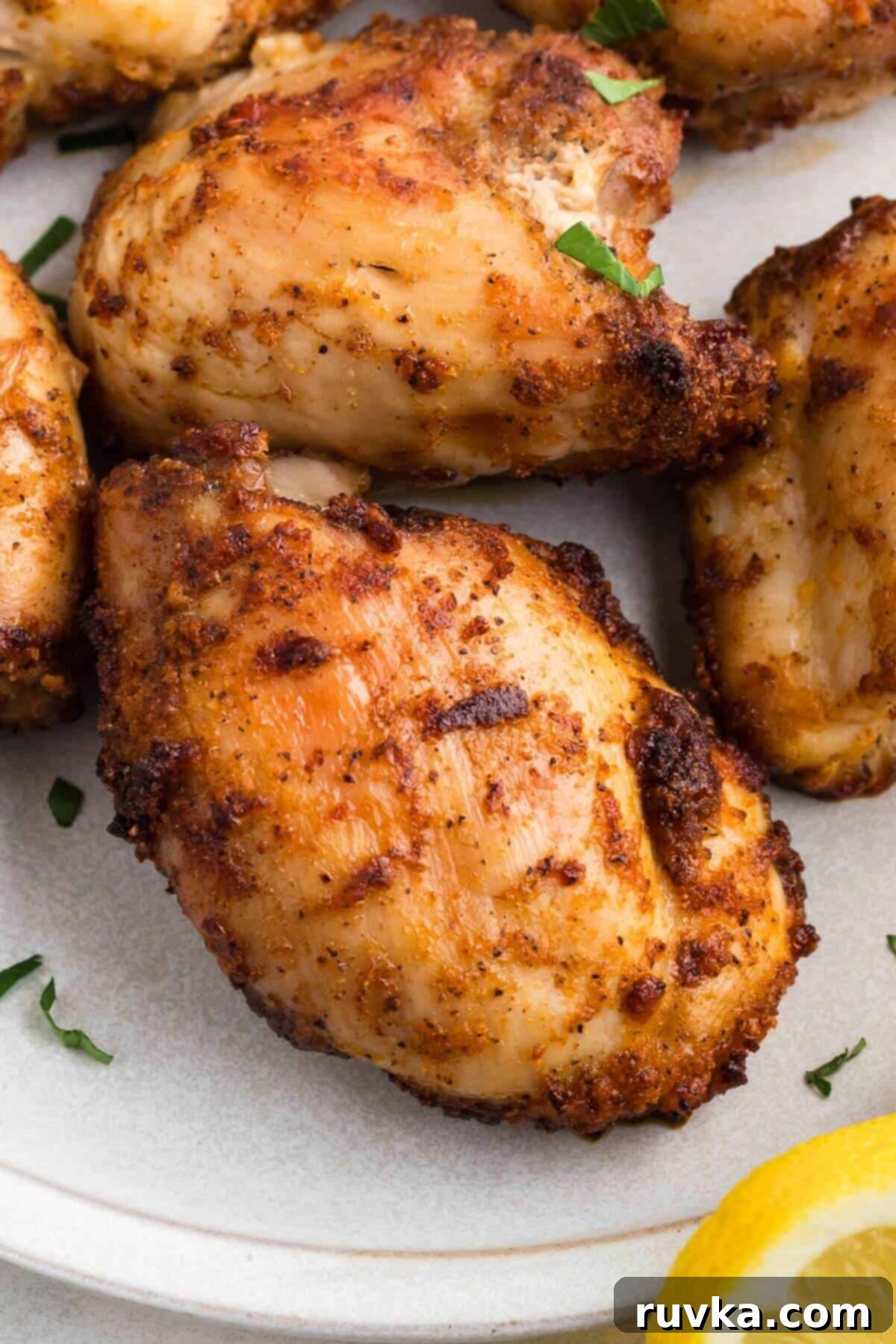 Freezer to Fabulous Air Fryer Chicken Thighs 8 Golden crispy chicken thighs on a white plate with a lemon slice for garnish.