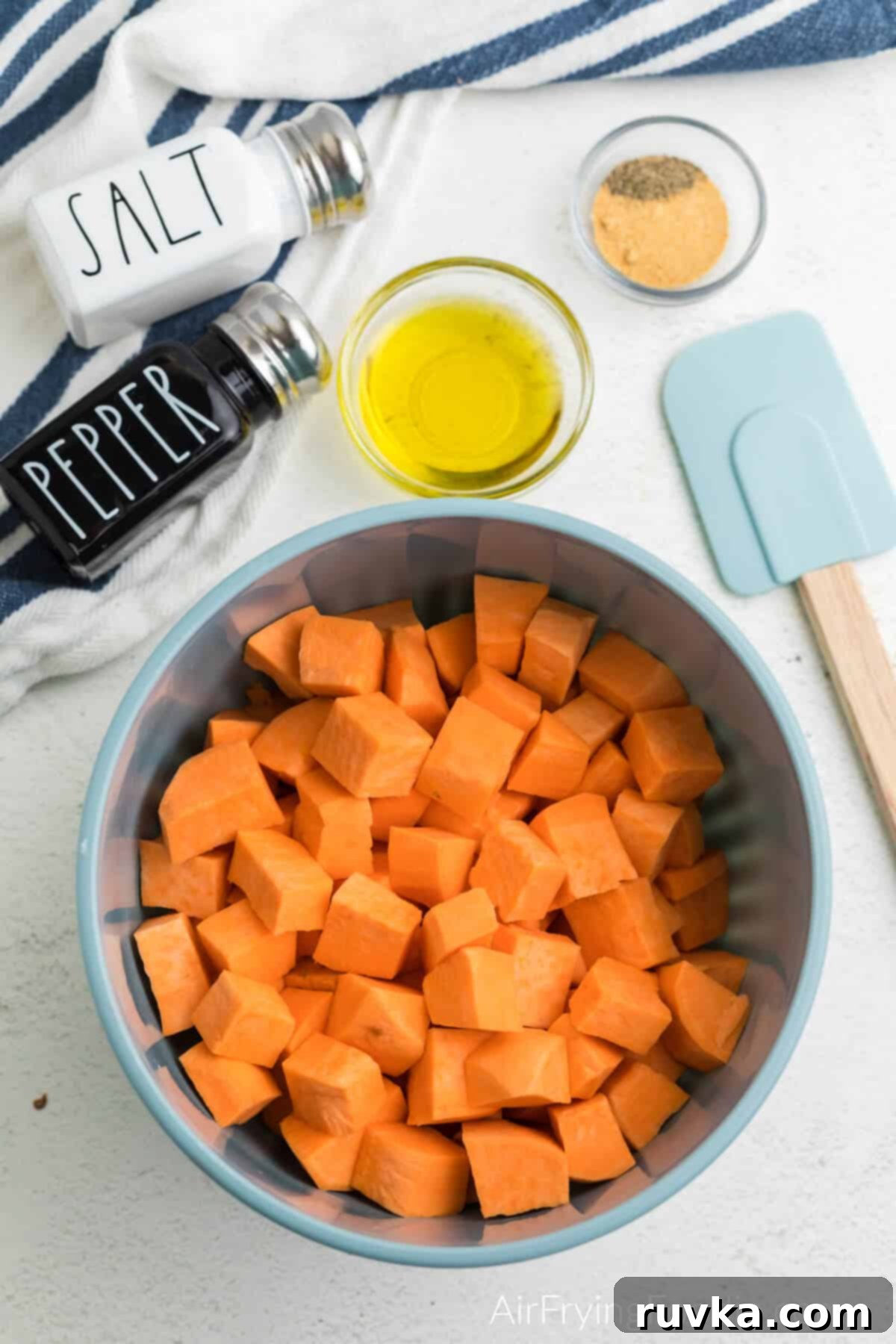 Crispy Air-Fried Sweet Potato Cubes 6 Sweet potato cubes in a mixing bowl with olive oil and seasoning and a spatular off to the side.