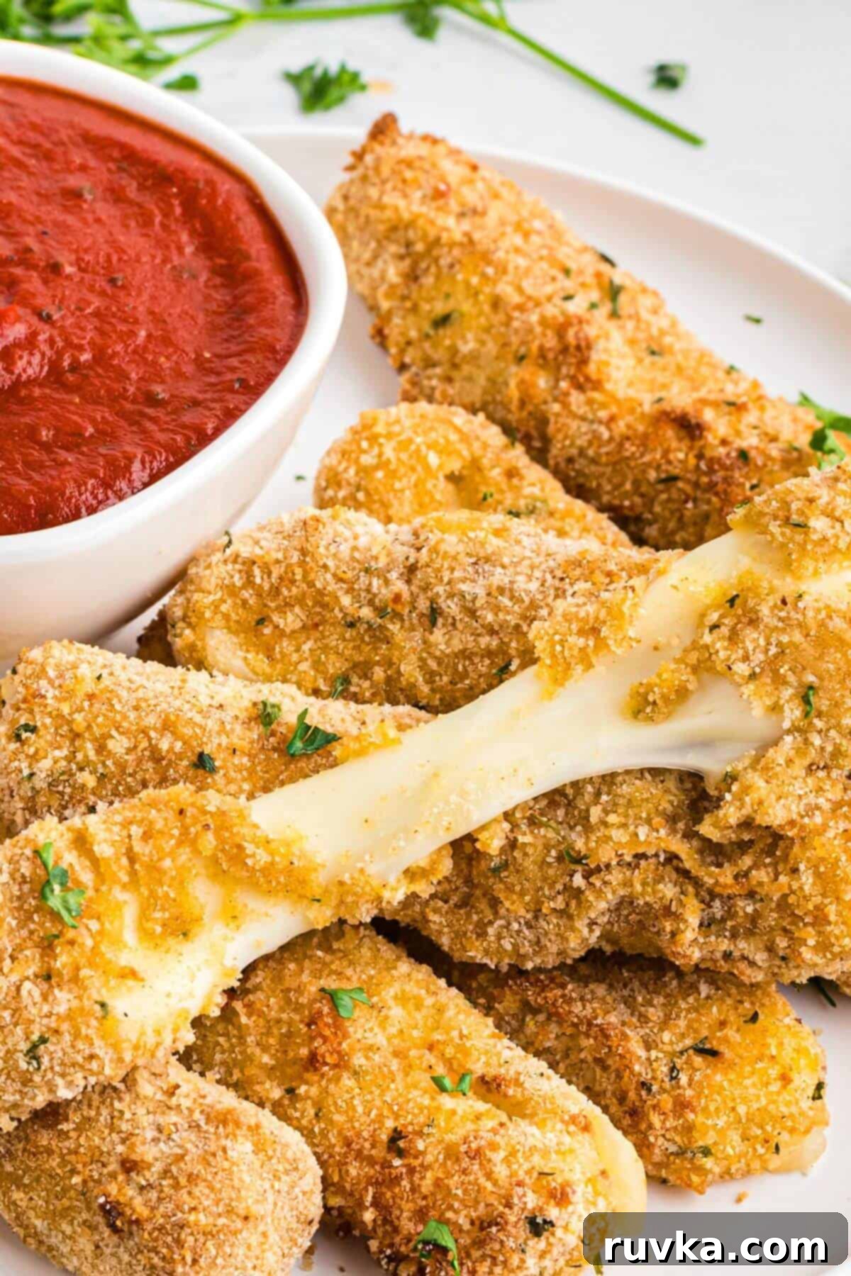 Crispy Air Fryer Mozzarella Sticks 2 Golden breaded mozzarella cheese sticks stacked on a white plate with marinara sauce.