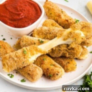 Crispy Air Fryer Mozzarella Sticks 9 Golden breaded mozzarella cheese sticks stacked on a white plate with marinara sauce.